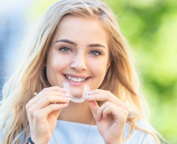 Young woman smiling while holding a clear aligner
