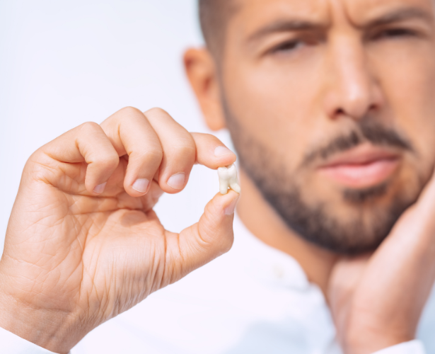 Man holding an extracted tooth and touching his jaw in pain