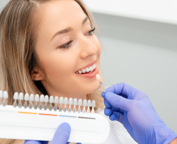 Dentist holding a veneer shade guide next to a patient’s teeth
